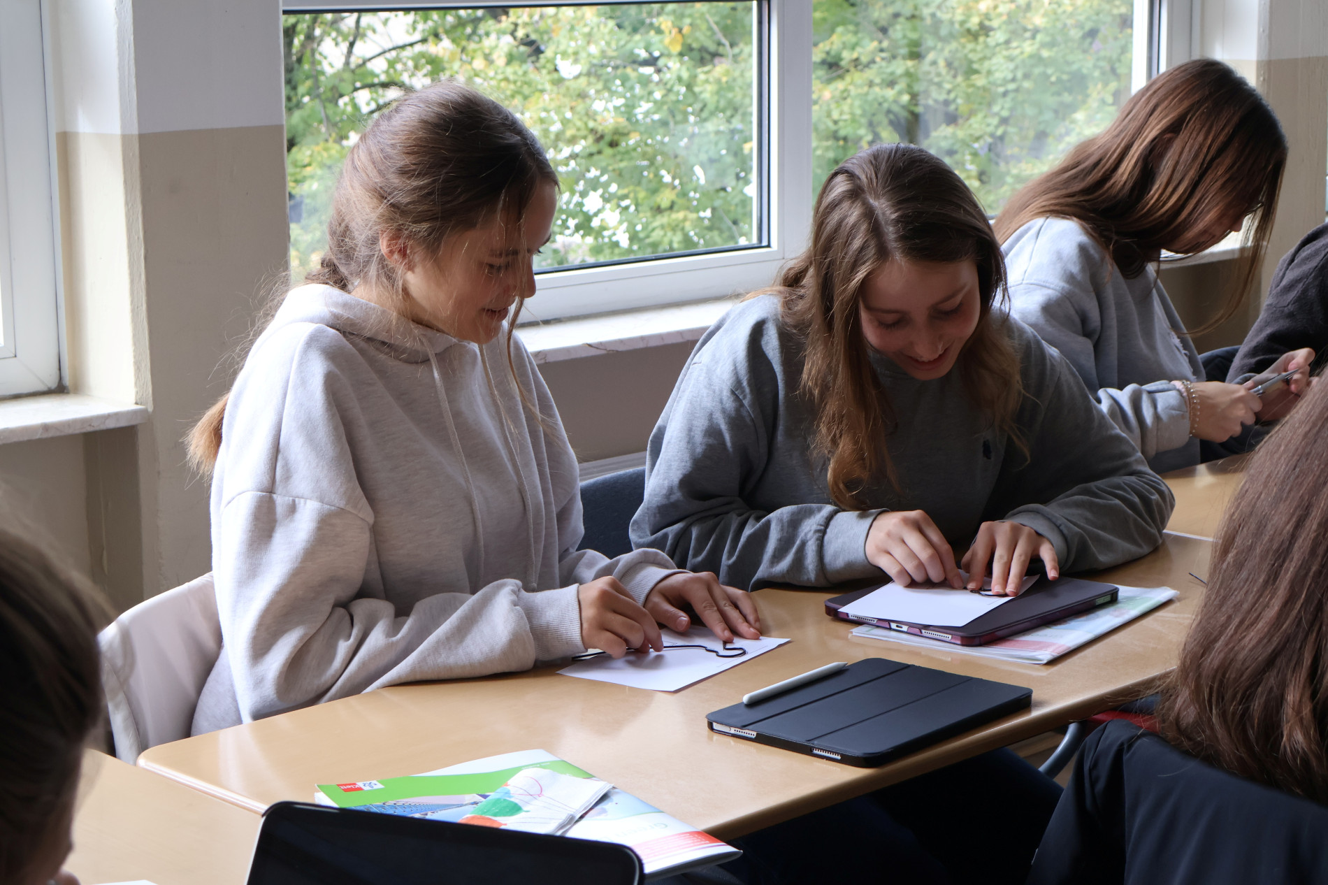 Zwei Schülerinnen der 9. Klasse bearbeiten konzentriert eine praktische Aufgabe mit Papier und Draht an ihren Schultischen. Zwei Schülerinnen der 9. Klasse bearbeiten konzentriert eine praktische Aufgabe mit Papier und Draht an ihren Schultischen.