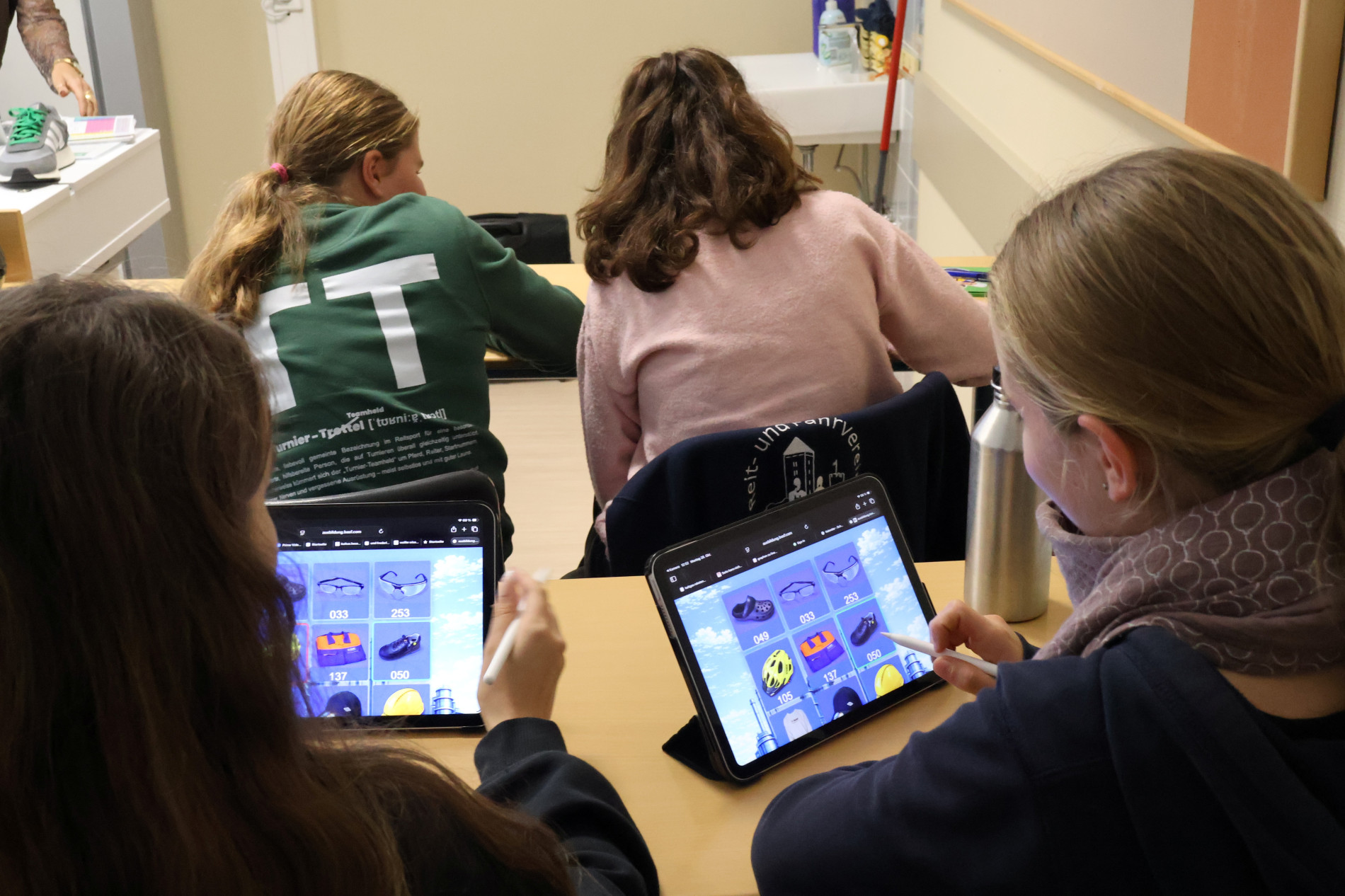 Schülerinnen arbeiten an Tablets mit einer digitalen Aufgabe, bei der verschiedene Gegenstände auf dem Bildschirm zu sehen sind. Schülerinnen arbeiten an Tablets mit einer digitalen Aufgabe, bei der verschiedene Gegenstände auf dem Bildschirm zu sehen sind.
