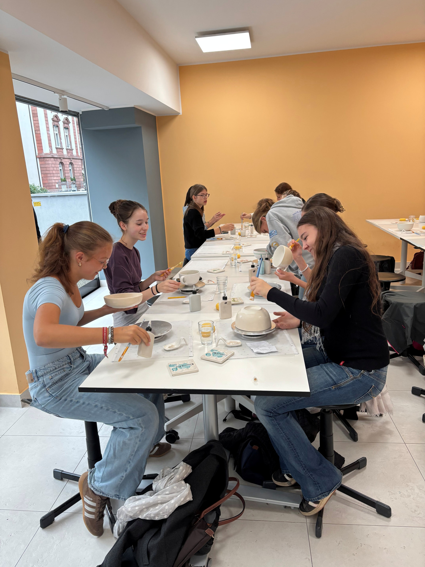 Schülerinnen der Klasse 8a bemalen gemeinsam verschiedene Keramikstücke an einem langen Tisch im Keramikzauber Frankfurt.