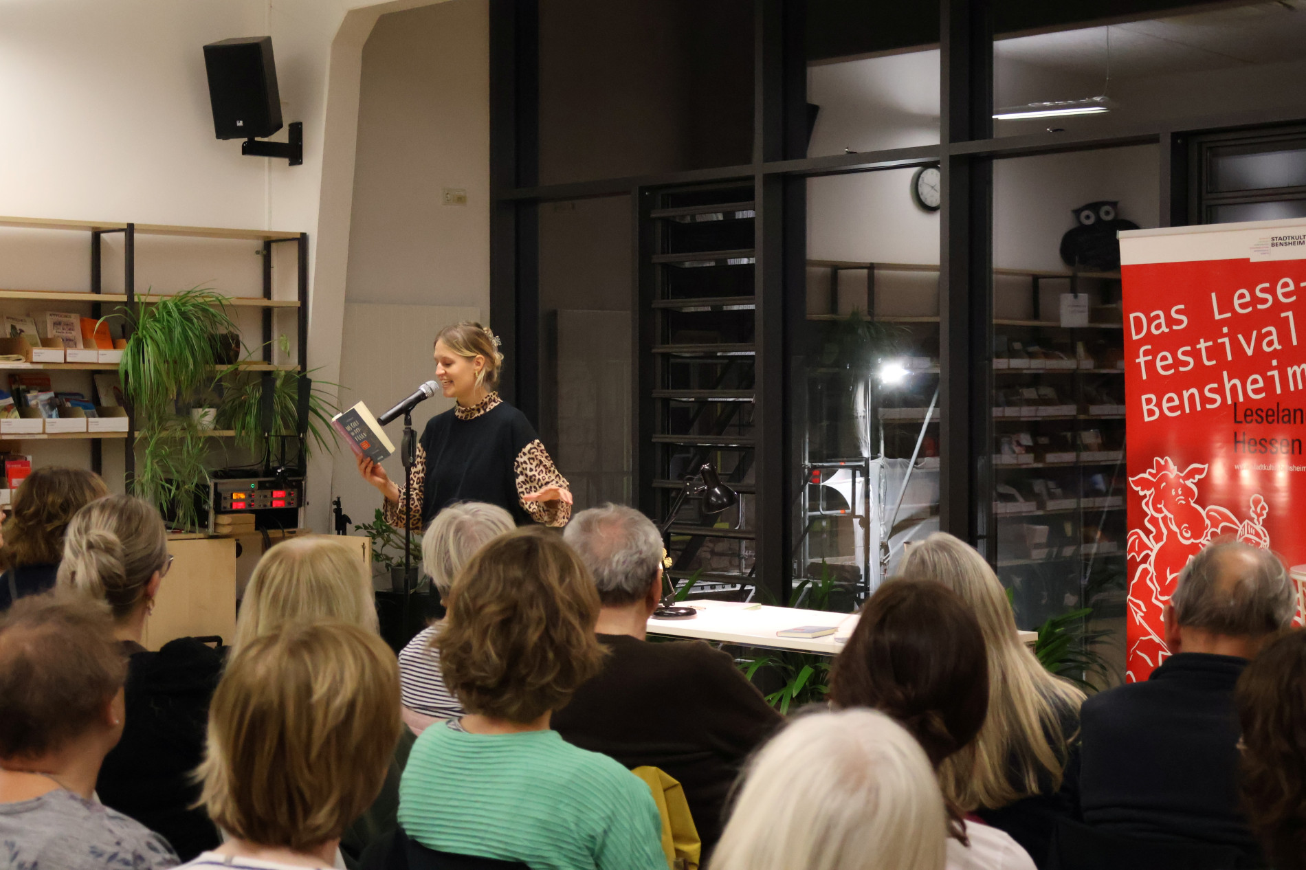 Leah Weigand liest mit einem Buch in der Hand vor zahlreichen Gästen. Im Hintergrund ist das rote Banner des Bensheimer Lesefestivals zu sehen. Leah Weigand liest mit einem Buch in der Hand vor zahlreichen Gästen. Im Hintergrund ist das rote Banner des Bensheimer Lesefestivals zu sehen.